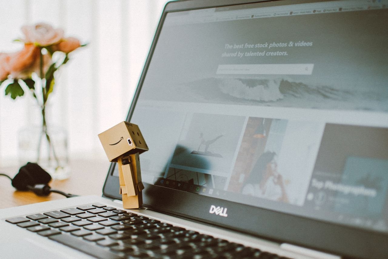 About A small toy figure stands on a laptop keyboard with flowers in the background.