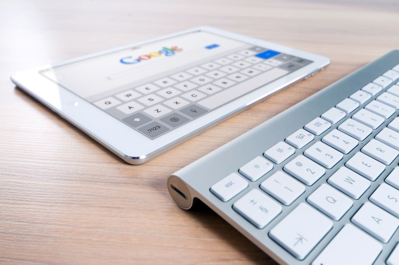 The Art of Drawing Readers In: Your attractive post title goes here A modern tablet displaying a search engine logo next to a wireless keyboard on a wooden desk.